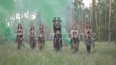 一群身着化妆和神秘服装的女舞者在彩烟中翩翩起舞。 森林仙女，干柴
